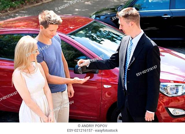 Salesman Giving Key To Couple By Car