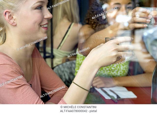 Young woman having drink in cafe with friends
