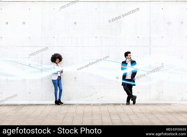 Businesswoman using mobile phone while standing by man with glowing wave pattern on footpath