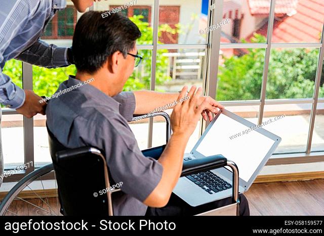 Asian senior disabled businessman in a wheelchair with laptop computer discuss together with team in office. Old father man sitting wheelchair and his son...