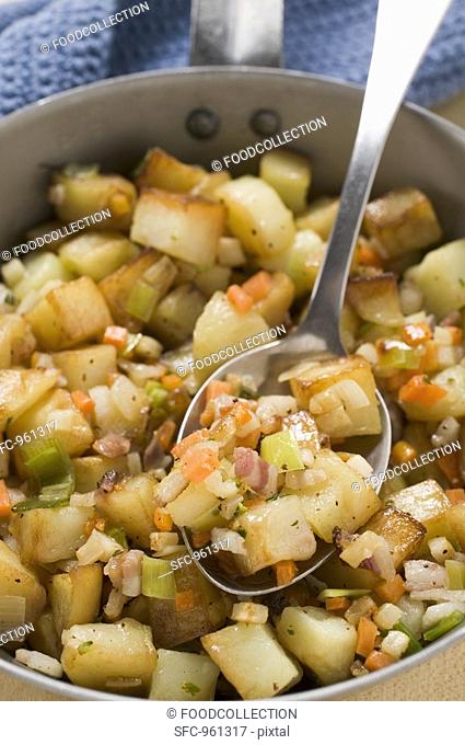 Fried potatoes with vegetables & bacon in frying pan with spoon