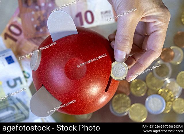 ILLUSTRATION - 23 October 2023, Saxony, Leipzig: A woman puts a 1 euro coin into a piggy bank. October 30, 2023 is World Savings Day