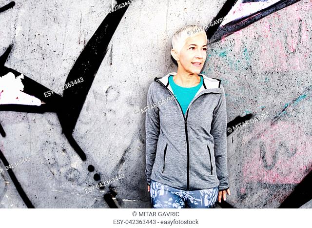 Senior Woman Relax After Running, Leaning On The Gray Concrete Wall. Short Hair, Sports Clothes , Looking At The Side