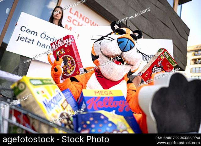 12 August 2022, Berlin: An activist in a tiger costume sits in front of the Ministry of Agriculture with two packs of breakfast cereal at a demonstration for...