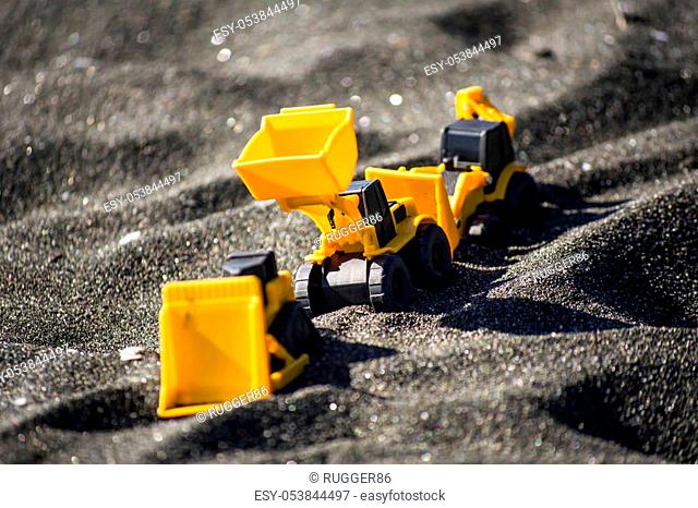 Toy construction machinery in black sand. Yellow and black colors toy machines. Bulldozer, loader, excavator