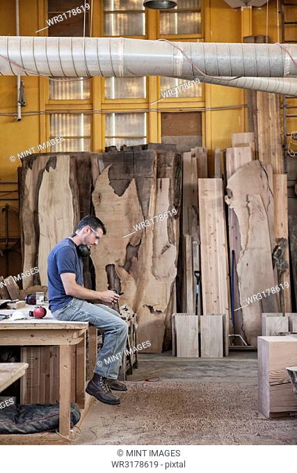 Caucasian man factory worker taking a break checking phone messages in a woodworking factory