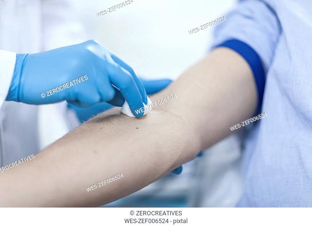 Doctor cleaning patient's arm with cotton pad before injection