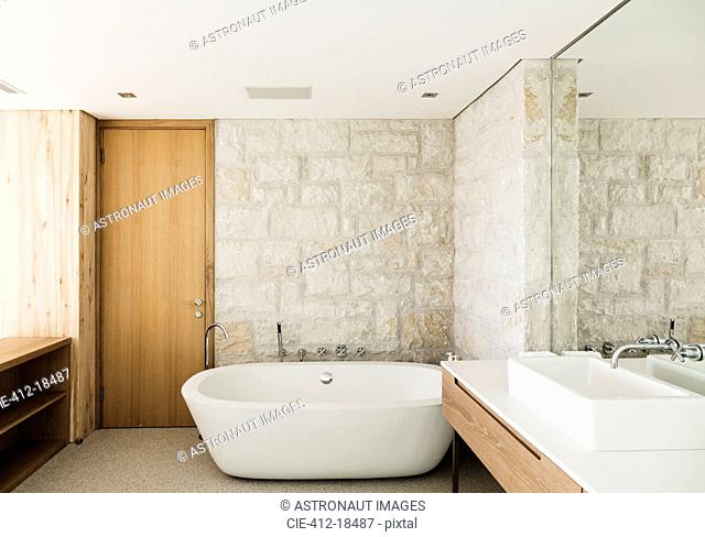 Stone walls behind soaking tub in modern bathroom