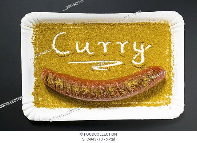 A currywurst in curry powder on a paper plate