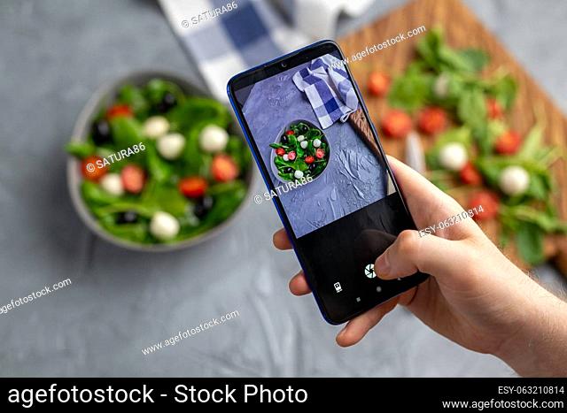 Man shooting fresh vegetable salad with mozzarella and spinach on cell phone camera. Cooking, blogging and healthy eating