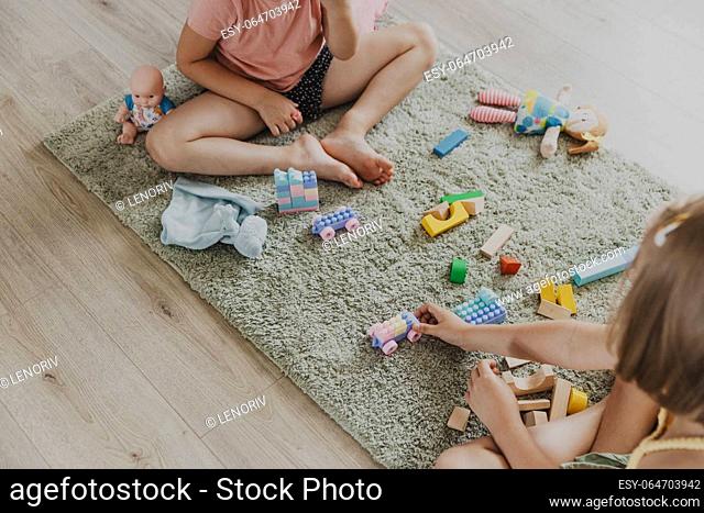 Children playing with colorful plastic toy colourful train. Kids sitting on carpet indoors at sunny white home bedroom or kindergarten, nursery
