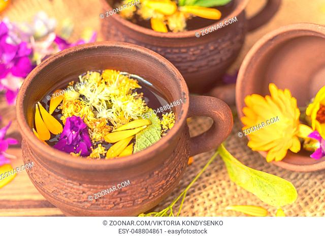 Two ceramic cups of healthy herbal tea with decoction of dry and fresh flowers on dark aged rustic wooden background. Shallow depth of field