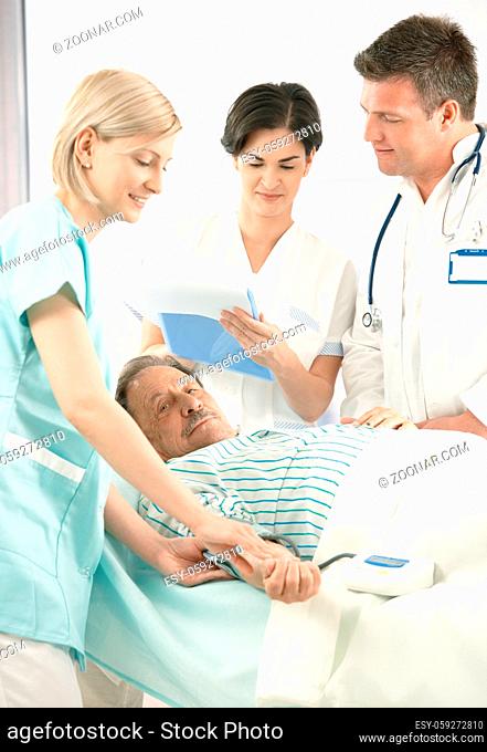 Doctors and nurse examining old patient in hospital, nurse measuring blood pressure, doctor taking notes