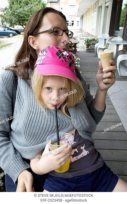 Chilly daughter wrapped inside mom's sweater sipping her orange juice thru a straw age 6 and 34. Rawa Mazowiecka Central Poland