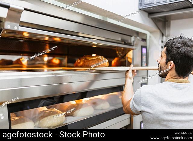 Baker baking bread in oven at bakery