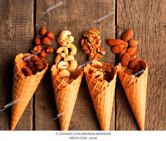 Ice cream cone with organic hazelnuts, cashews, almonds and walnuts on a rustic wooden table
