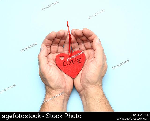 male hands holding red heart on a blue background, close up, top view