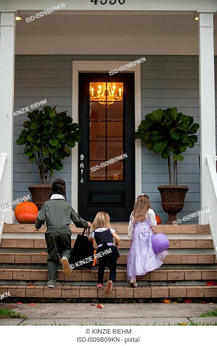 Rear view of boy and sisters trick or treating moving up porch stairway