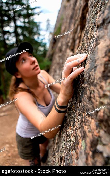 A selective focus shot as a thrill seeking woman attempts rock climbing without safety gear or equipment, wearing a black cap and grey vest, with copy space