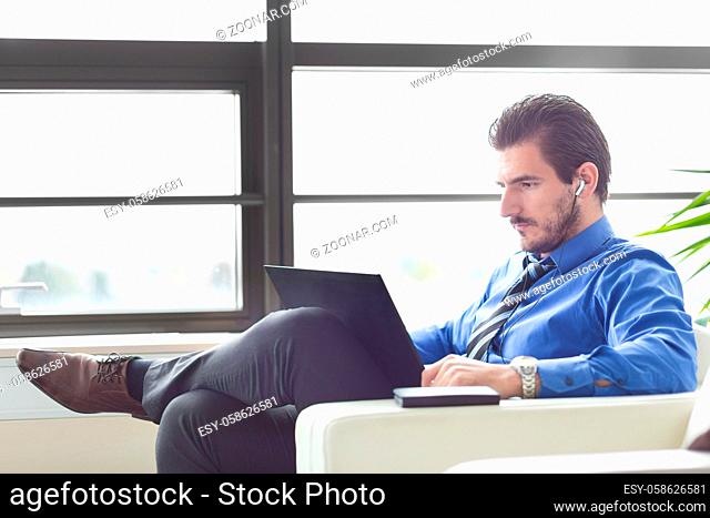 Busy, focused businessman in office working on his laptop wearing headphones. Side view