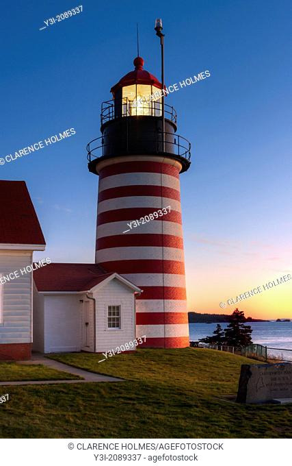 The rising sun brightens the eastern sky across Quoddy Narrows from West Quoddy Head Light in Lubec, Maine. The lighthouse protects mariners passing the...