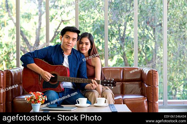 Young lovers spend time together on holidays in the living room. The young man wears comfortable clothes, play a guitar