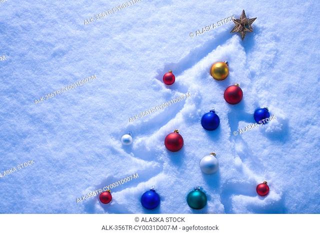 Christmas tree outlined in a fresh blanket of snow with multi-colored bulb ornaments covering tree and gold star at top winter Alaska