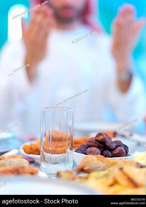 young arabian muslim man making traditional prayer to God, keeps hands in praying gesture before iftar dinner with family representing modern islam fashion and...