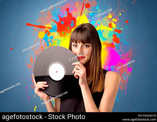 Young lady holding vinyl record on a grey background with colorful splashes behind her