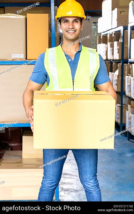 Portrait of Indian warehouse worker hold cardboard box packaging in warehouse distribution center environment. Using in business warehouse and logistic concept