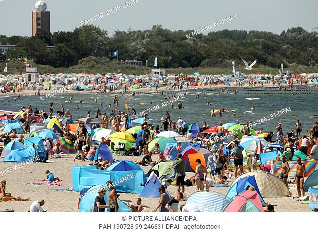 26 July 2019, Mecklenburg-Western Pomerania, Rostock: The Baltic Sea beach of Warnemünde is very busy. Beach shells and parasols dominate the picture