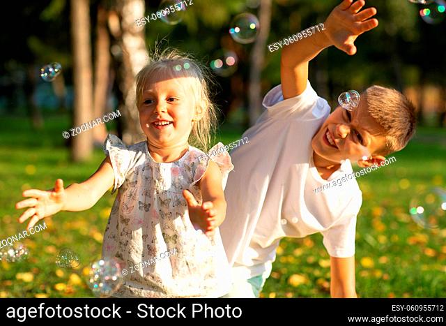 Cute little children boy and girl blowing bubbles in autumn park on sunny day