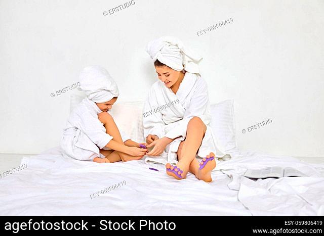 mother and daughter in white bathrobes with pedicure sponge on fingers. mom spending time together with kids