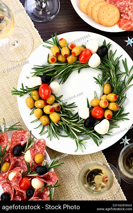 An appetizer of rosemary stuffed with olives with baby mozzarella and cherry tomatoes. Made in the form of a Christmas wreath