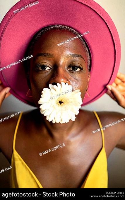 Woman with white flower in mouth wearing pink hat at home