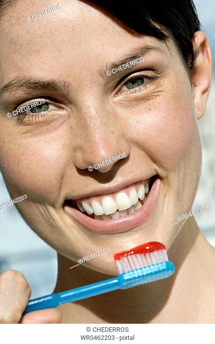 Portrait of a young woman holding a toothbrush with toothpaste and smiling