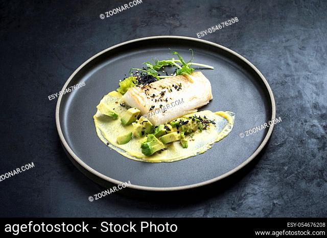 Gourmet fried cod fish filet with caviar, avocado slices and mustard mango creme as closeup on a modern design plate