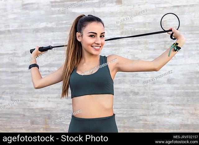 Slim athlete with jump rope exercising in front of wall