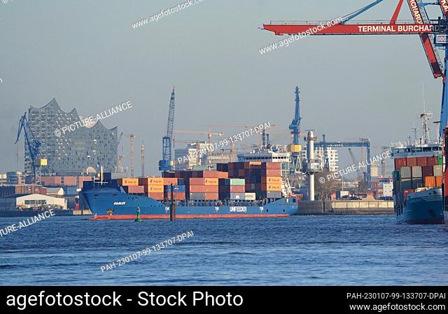 PRODUCTION - 03 January 2023, Hamburg: A small container ship leaves a container terminal in the port. The Port of Hamburg on the Elbe is a universal port for...