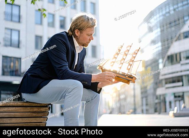 Businessman sitting on a bench in the city holding model ship