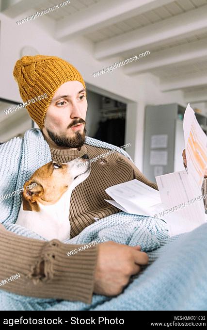Wickede, NRW, Deutschland. Ein junger Mann trÇÏgt eine StrickmÇ¬tze Zuhause mit einem Hund Jack Russell Terrier schaut erstaunlich auf eine Rechnung an