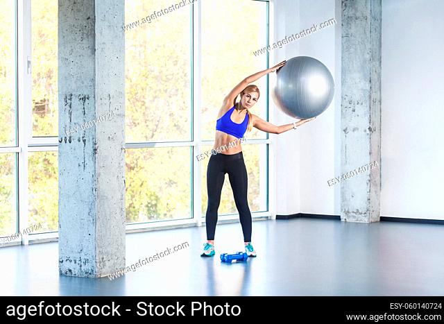 Blonde woman tilt side, holding fit ball. Studio shot