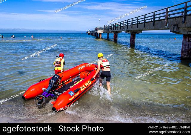 15 July 2021, Mecklenburg-Western Pomerania, Prerow: Lifeguards Nils Frechen and Nils Lerner from the DLRG water rescue pull the lifeboat into the water next to...