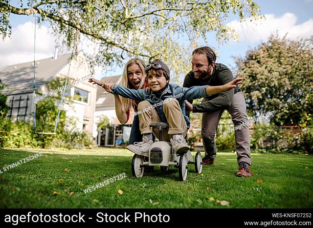 Boy sitting on toy car, pretending to fly, parents encourageing him