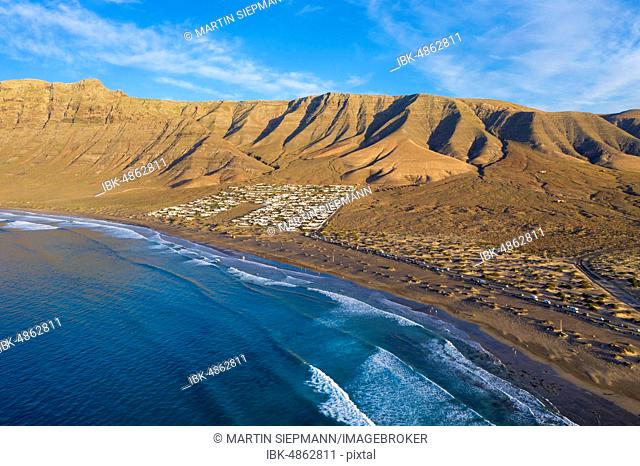 View on beach Playa Famara with bungalows and mountain range Risco de Famara, at Caleta de Famara, drone shot, Lanzarote, Canary Islands, Spain
