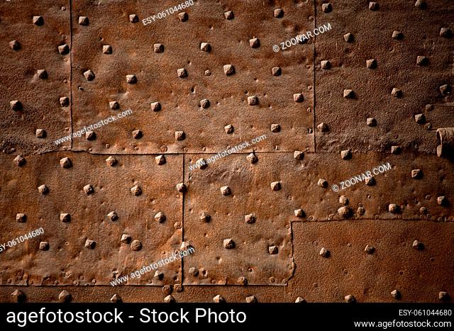Old wall covered with sheets of rusty iron with rivets. Abstract retro background