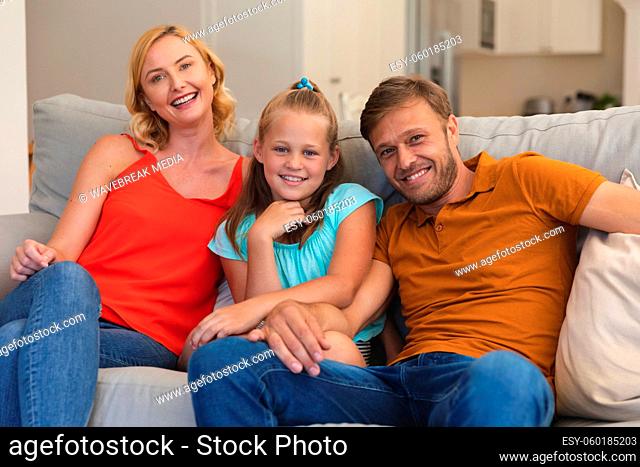 Portrait of caucasian couple with daughter sitting on couch and smiling at home