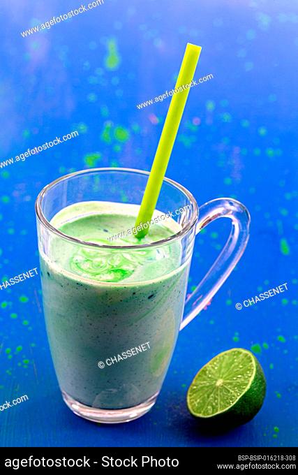 Close up of a glass of spirulina smoothie with a lime on a blue background