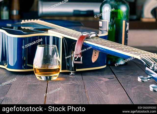 Guitar side view, strings and fingerboard with glass of alcohol on table