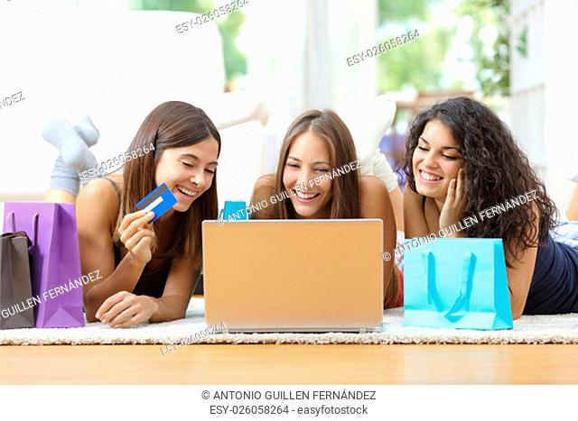 Three friends shopping online with credit card and laptop lying on the floor at home